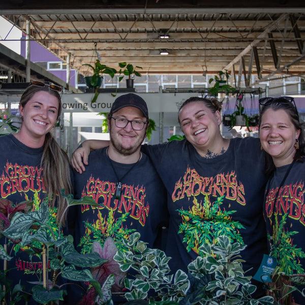 Four people wearing 'Grown Together' t-shirts in a greenhouse setting.