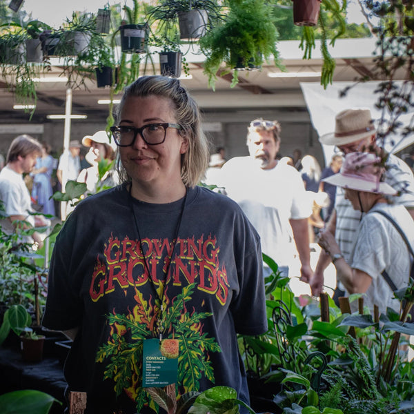 Person wearing a colorful t-shirt with text in an outdoor setting with plants and people.